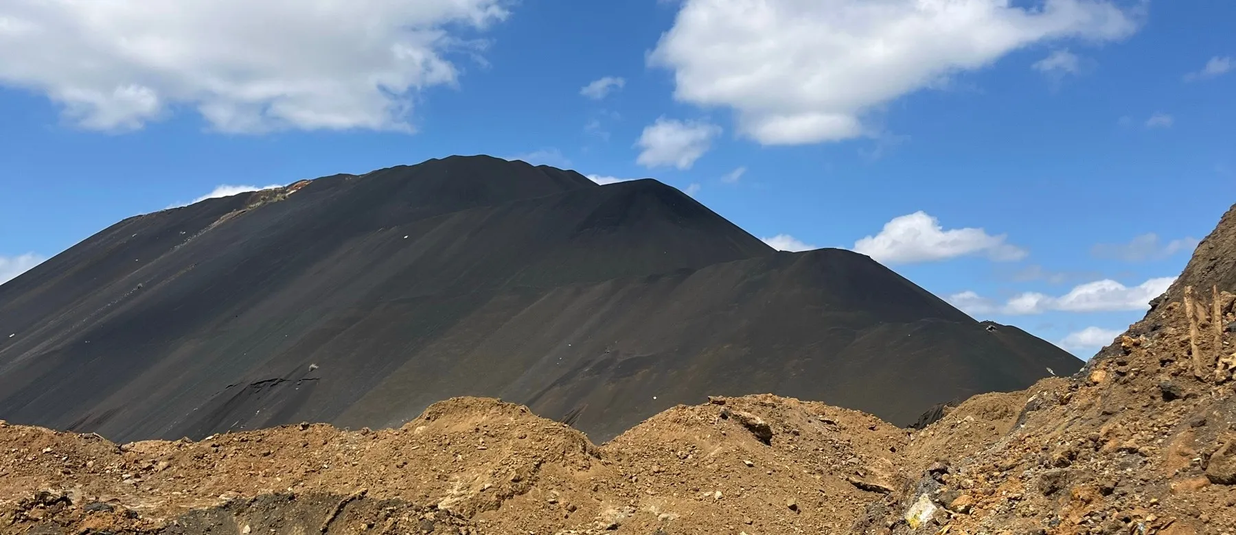 Mounds of stockpiled material in front of a dark dump hill at the Selebi-Phikwe site